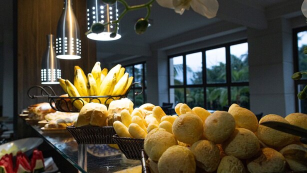 Tarjolla on monipuolinen buffet, jossa on erilaisia ruokia, kuten leipää ja banaaneja, ja sen yläpuolella on modernit riippuvalaisimet.
