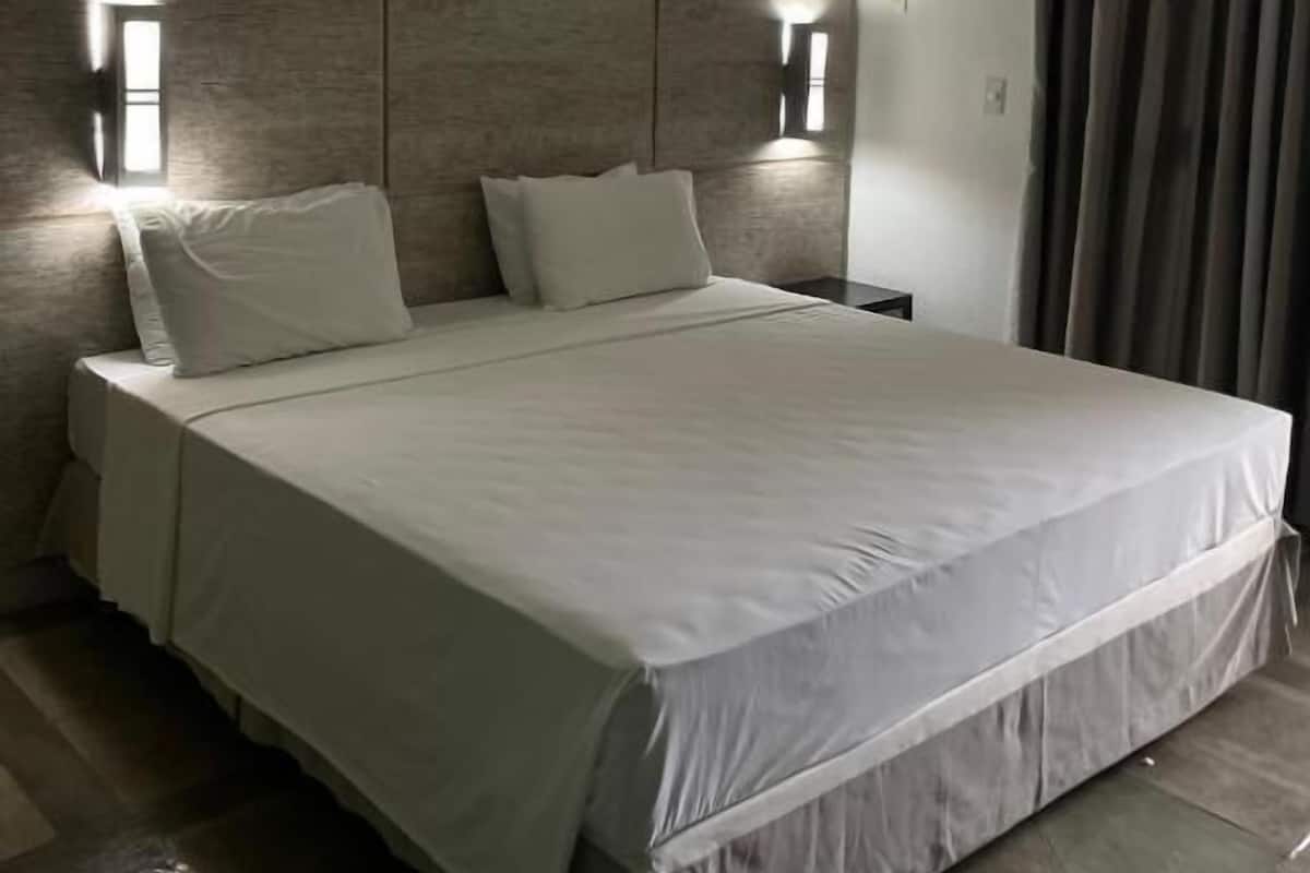 A hotel room with a large bed, two wall-mounted lights, an air conditioning unit, and a window with curtains.