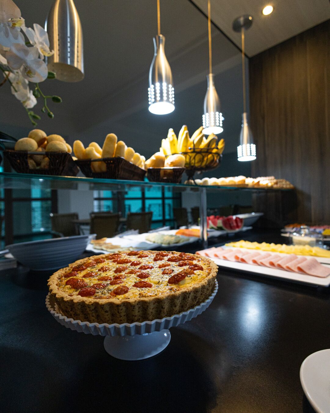 A buffet with various food items including a quiche, bananas, and pastries.