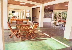 An indoor patio area with a wooden table and chairs, a kitchen in the background, and a view of trees through the window. - Araguaia Hotel (Barra do Garcas)