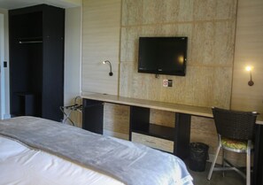 A hotel room with a bed, a desk with a chair, a television mounted on the wall, and a trash bin. - Araguaia Hotel (Barra do Garcas)