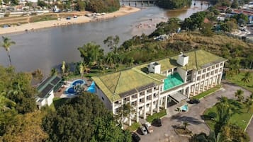 Un hotel grande con piscina, situado cerca de un río con un puente al fondo.