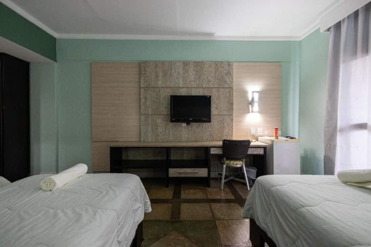 A hotel room with two beds, a desk, a chair, a television, and a window with curtains.