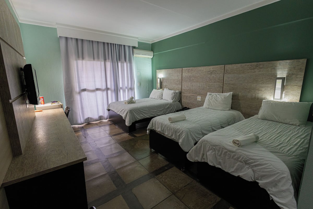 A hotel room with two single beds, a TV, a desk, and a window with curtains.
