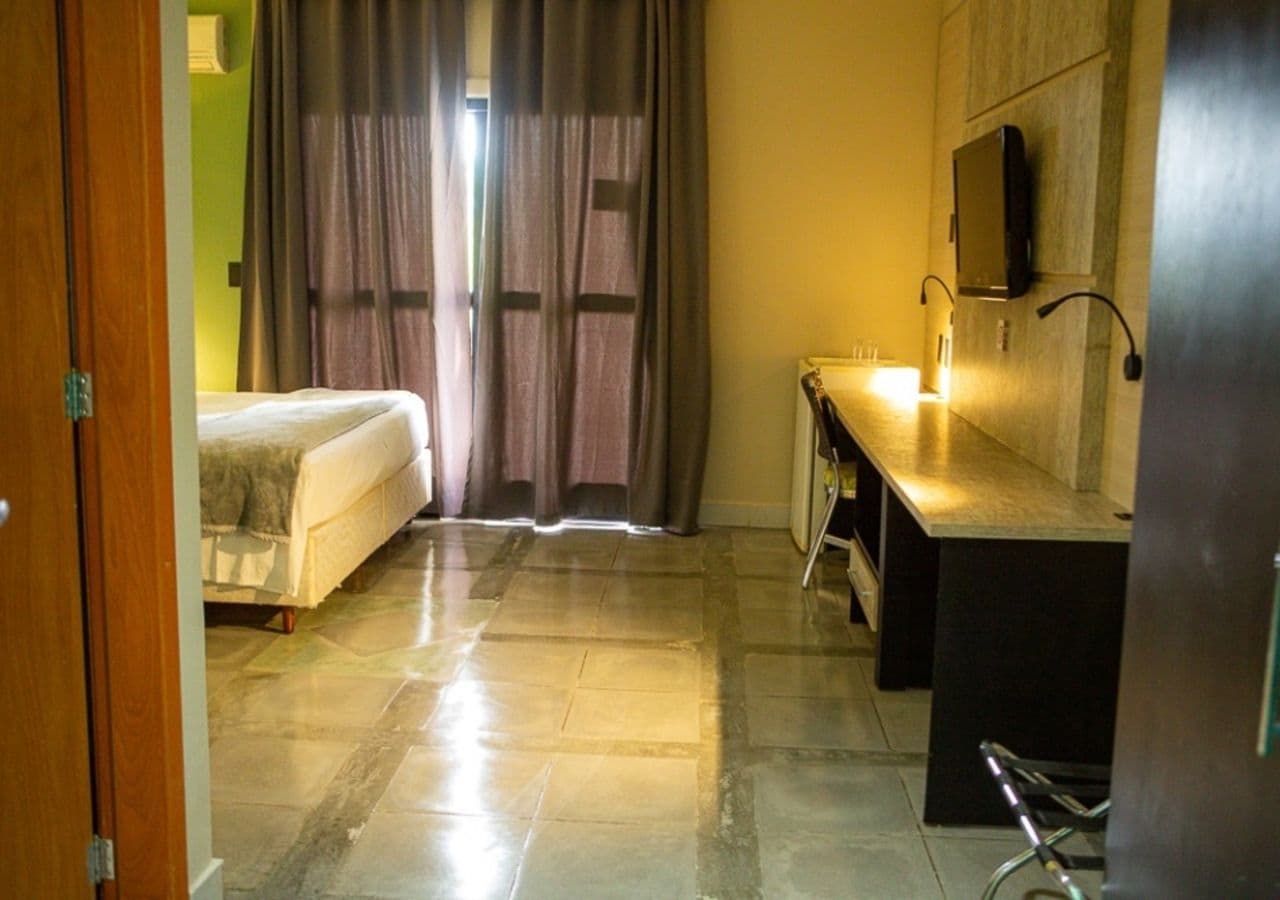 Une chambre d’hôtel équipée d’un lit, d’un bureau, d’une chaise, d’une télévision et d’une fenêtre avec des rideaux.