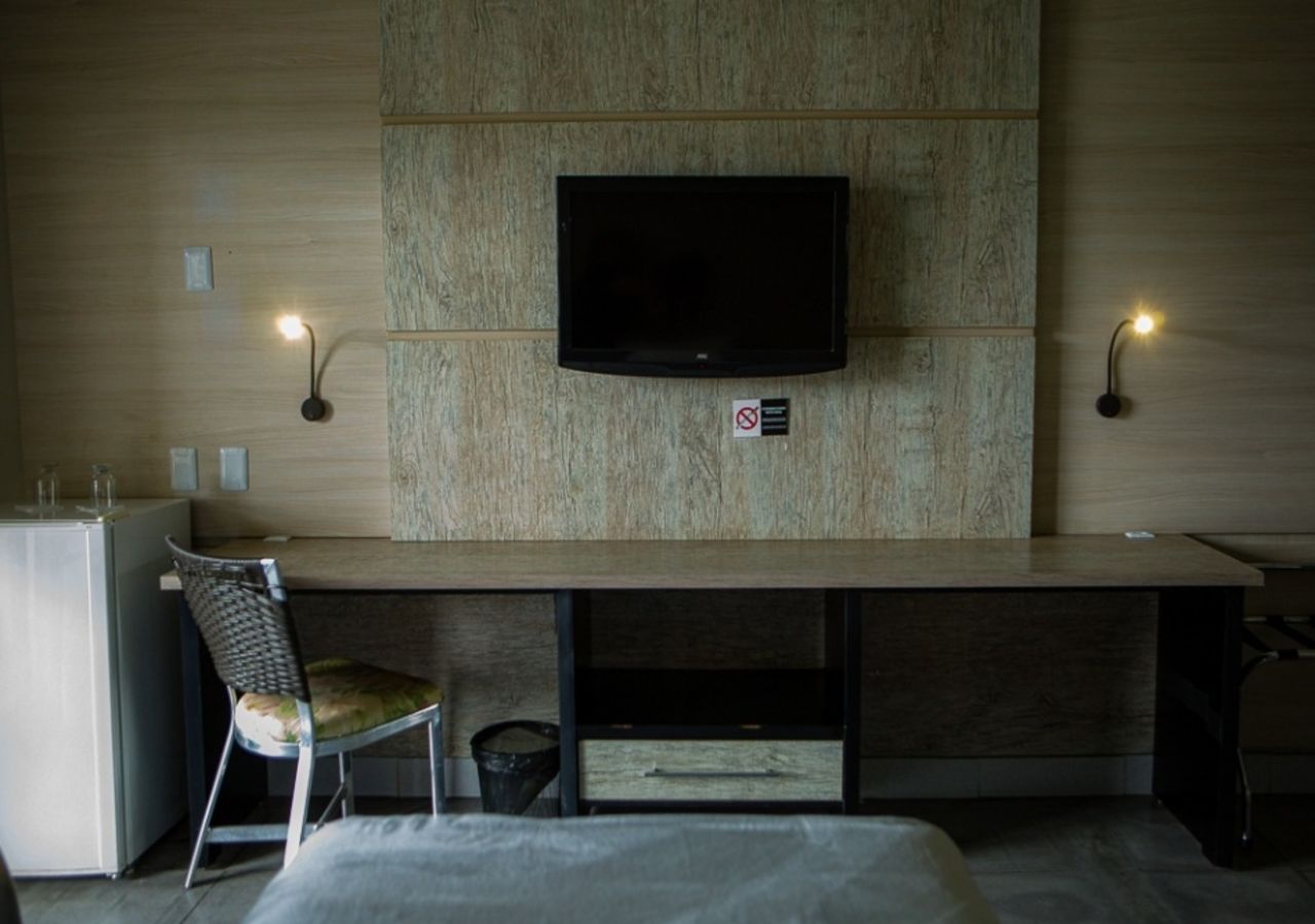 Habitación de hotel con televisión de pantalla plana en una pared de madera, un escritorio con una silla y dos lámparas de pared.