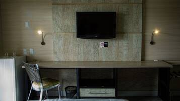 Habitación de hotel con televisión de pantalla plana en una pared de madera, un escritorio con una silla y dos lámparas de pared.