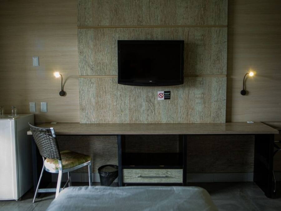 Habitación de hotel con televisión de pantalla plana en una pared de madera, un escritorio con una silla y dos lámparas de pared.
