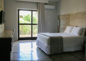A bedroom with a bed, a desk, and a window with a view of greenery. - Araguaia Hotel (Barra do Garcas)