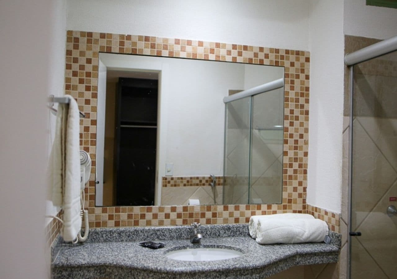 Casa de banho com bancada de granito, lavatório, espelho, toalha e cabine de duche com vidro.