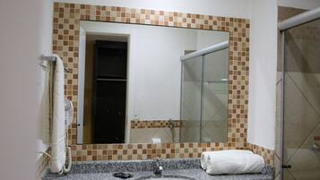 Casa de banho com bancada de granito, lavatório, espelho, toalha e cabine de duche com vidro.