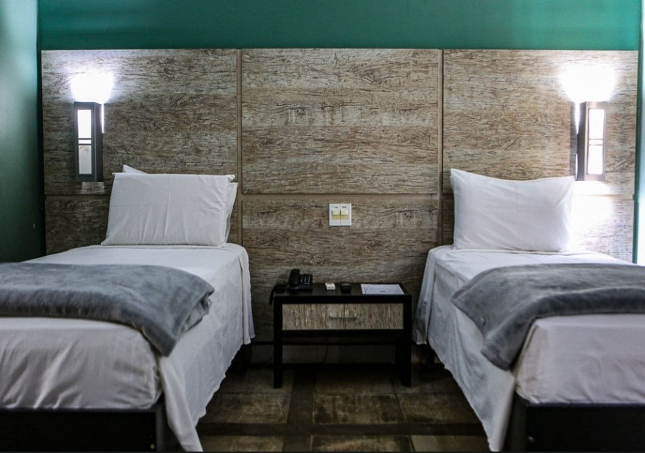 A room with two single beds, a small table, and a wall-mounted light fixture.