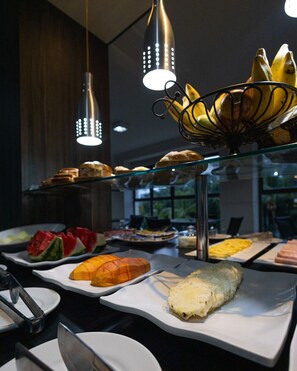 A buffet with various food items including fruits, pastries, and a bread roll.