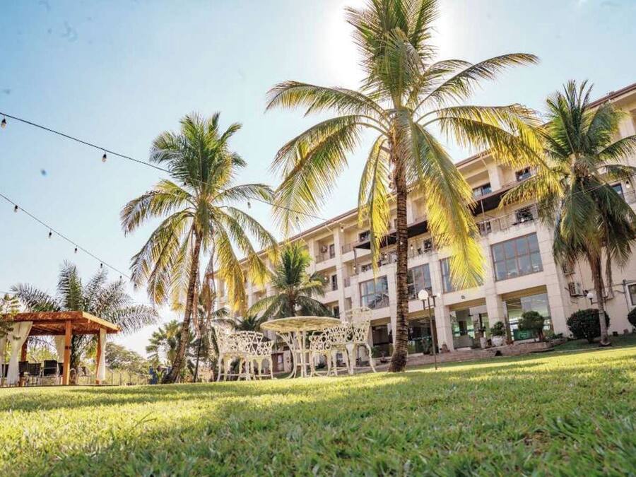 A hotel with a covered outdoor seating area, palm trees, and a building with multiple floors and balconies.