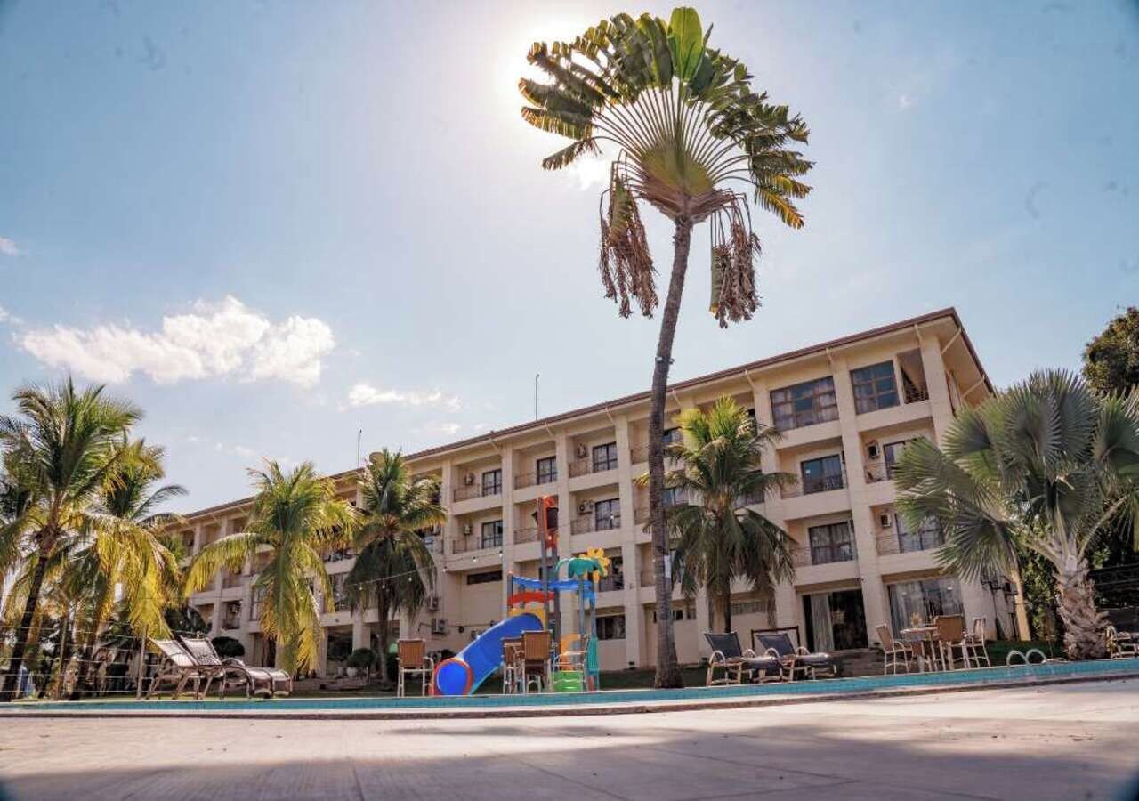Ein Hotel mit mehreren Etagen, einem Poolbereich inklusive Liegestühlen und Palmen.