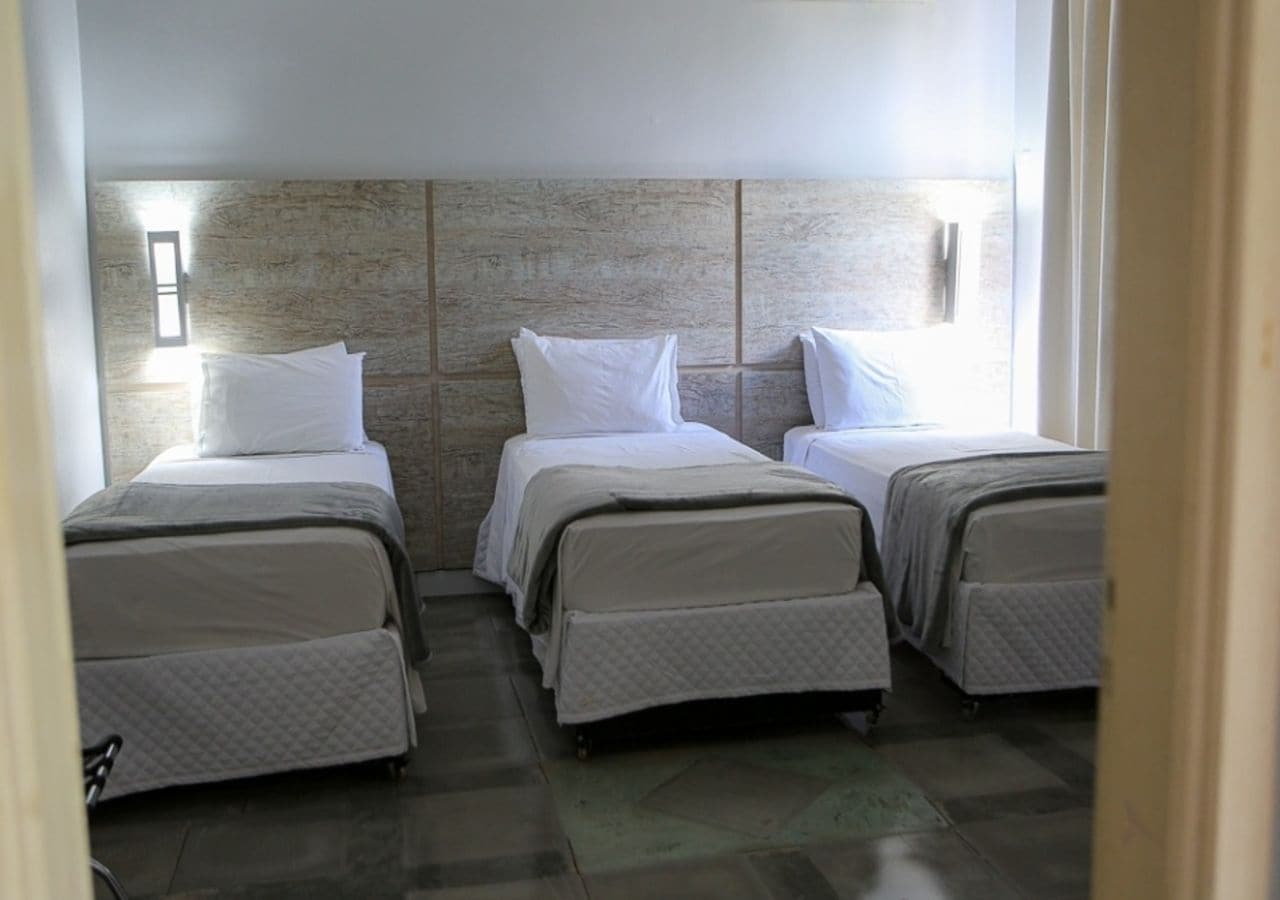 A hotel room with three beds aligned against a textured wall, each with a white bedspread and pillows.