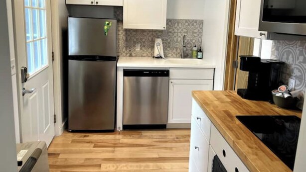 A compact kitchen with white cabinets, stainless steel appliances, a dishwasher, and a wooden countertop. - Mini Mod Apartment, Private- Parking (Winooski)