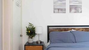 A bedroom with a bed, a nightstand, a lamp, and a potted plant. - Mini Mod Apartment, Private- Parking (Winooski)