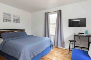Una camera da letto con un letto, una scrivania, una sedia, un televisore e una finestra con tende.