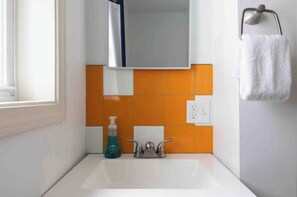 Un bagno con un lavandino bianco, piastrelle arancioni, uno specchio e un asciugamano su un portasci.