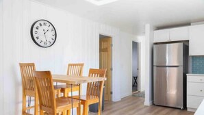 Eine moderne Küche mit einem Edelstahl-Kühlschrank, einem Holzes Esstisch mit Stühlen und einer Wanduhr.