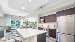 Una cocina moderna con una isla central, electrodomésticos de acero inoxidable y un sofá gris en la sala de estar.