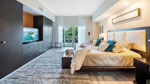 Une chambre moderne avec un grand lit, une télévision et un balcon donnant sur un espace verdoyant.