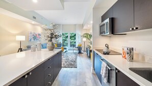 Une cuisine moderne avec des meubles sombres, un grand îlot central et une vue sur un espace de vie comprenant un canapé et une plante.