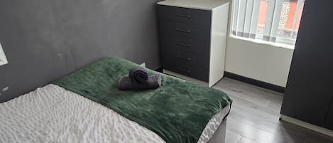 A bedroom with a bed, a dresser, and a window with blinds.