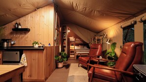 Een knus zolderkamer met houten plafond, een kitchenette, een bed en leren fauteuils.