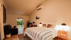 A bedroom with a bed, bedside table, and a nightstand. There is a door leading to a balcony.