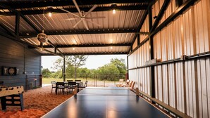 An indoor ping pong table with seating and a ceiling fan in a covered area with a view of the outdoors.