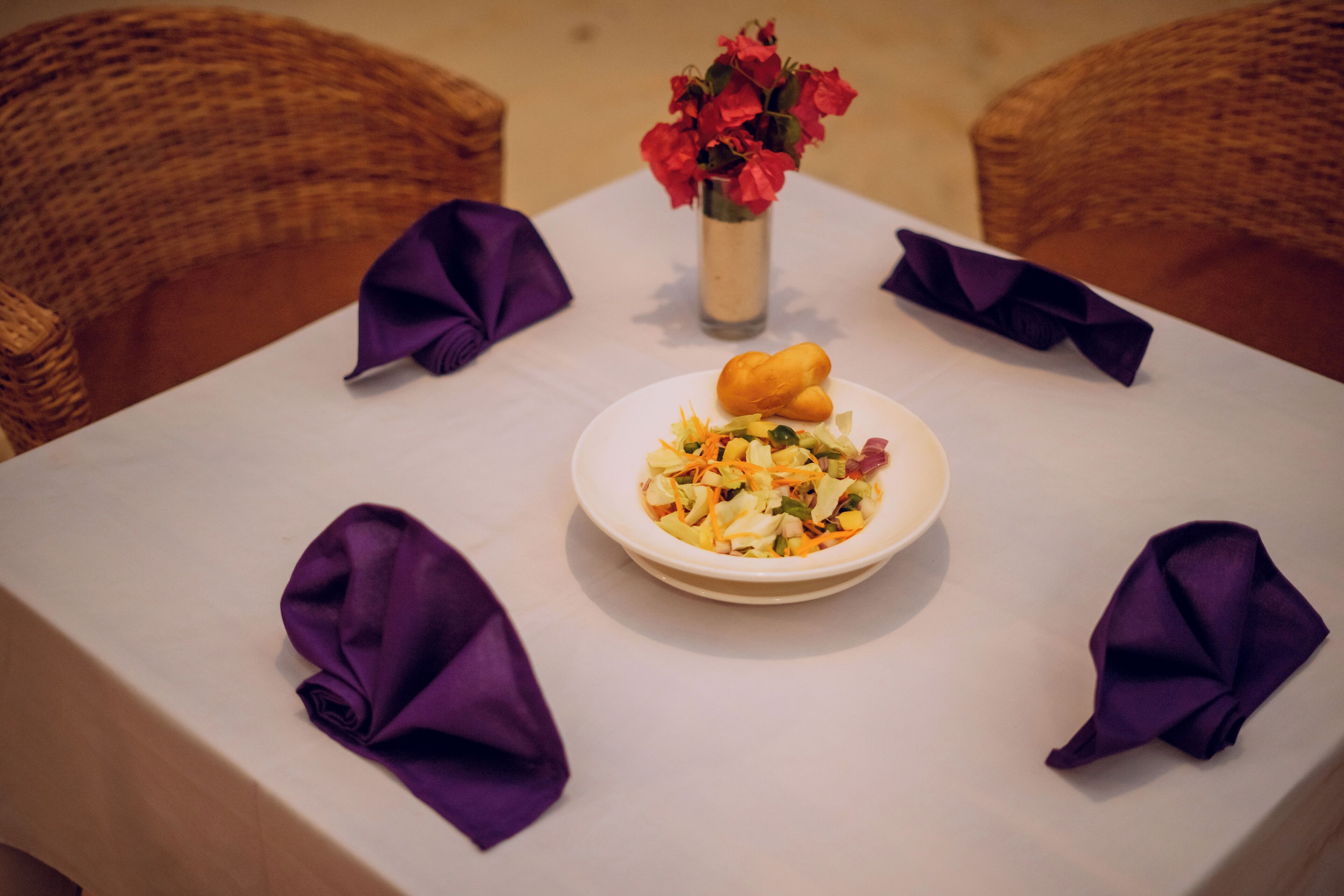 Une table à manger recouverte d’une nappe blanche, une assiette de nourriture et des serviettes violettes.