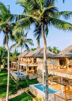 Un resort con varias cabañas, una piscina central y exuberante jardinería tropical.