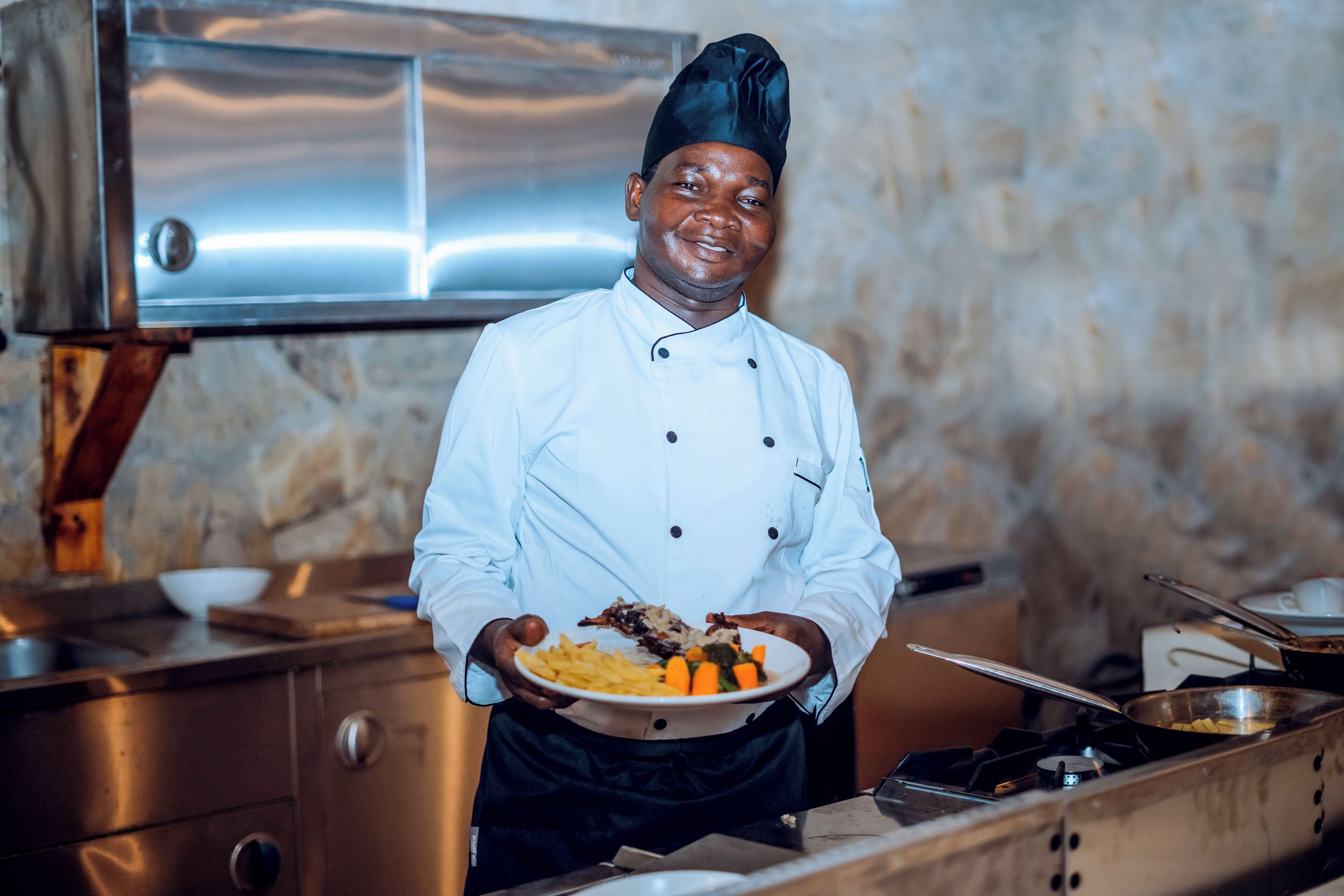 Un chef de cuisine dans une cuisine professionnelle, tenant une assiette de nourriture.