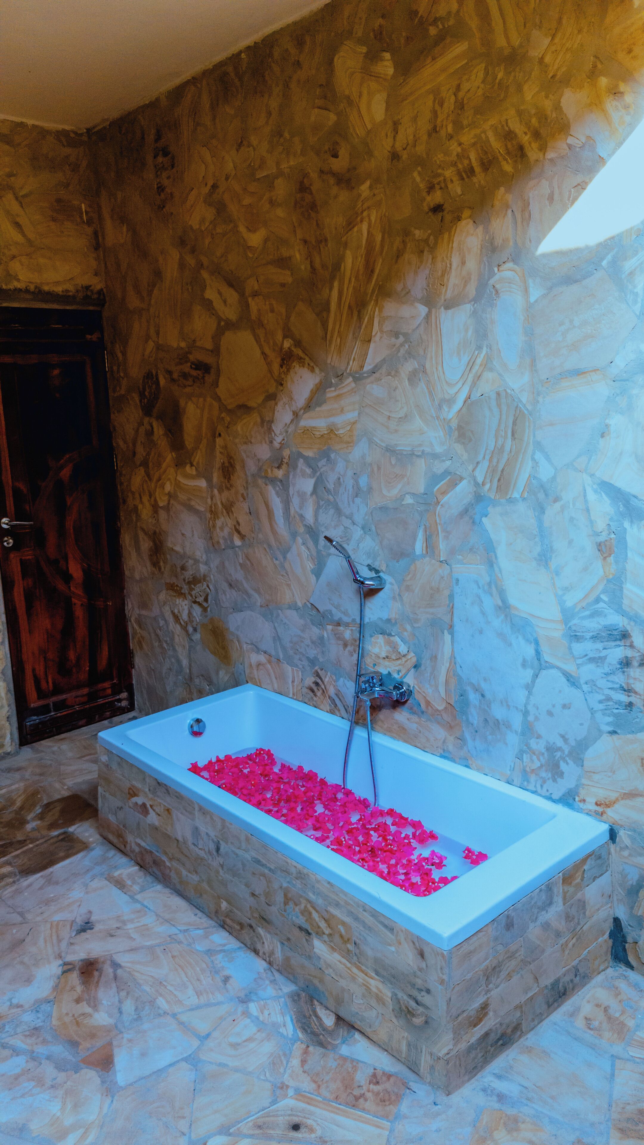 A stone-walled bathroom with a bathtub filled with rose petals.
