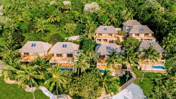 Un resort con varias villas de techo de paja rodeadas de exuberante vegetación y palmeras.