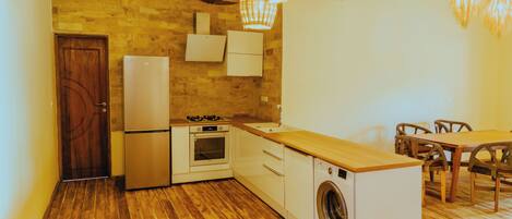 Una cocina compacta con piso de madera, lavadora integrada, refrigerador, horno y comedor con mesa y sillas de madera.