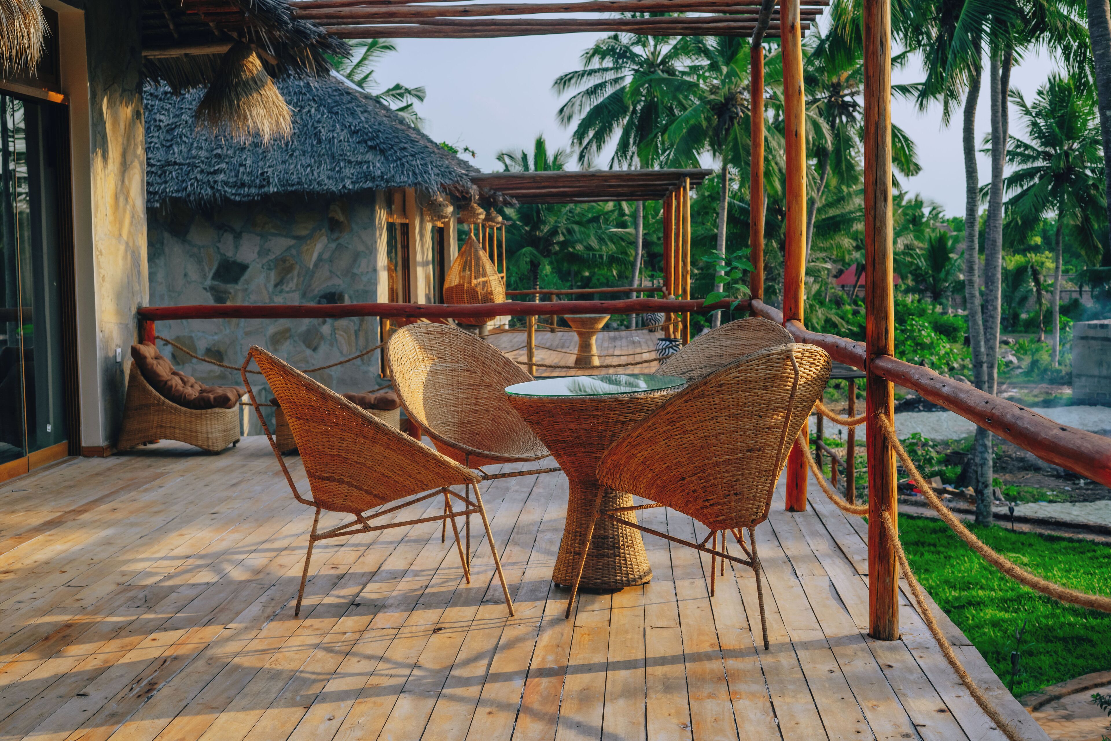A wooden deck with wicker furniture, a thatched-roof structure, and palm trees in the background.