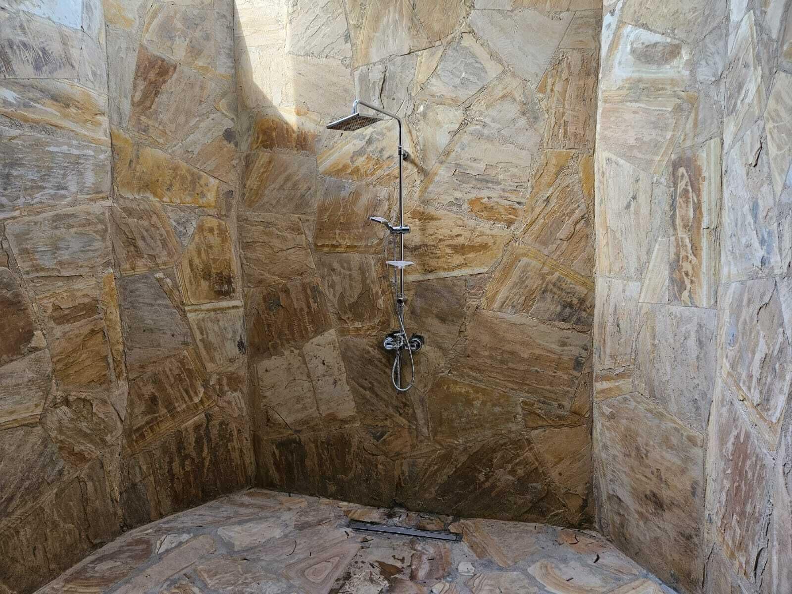 A stone-walled shower with a handheld showerhead and a fixed showerhead.
