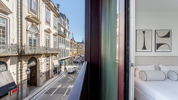 A modern hotel room with a large bed, a view of a busy street, and a balcony with ornate railings. - GuestReady - A peaceful home near downtown (Porto)