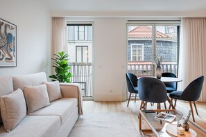 Un salon moderne avec un canapé, une table à manger et des chaises, une plante en pot et une vue sur un immeuble par la fenêtre.