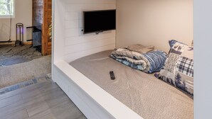 A room with a bunk bed, a mounted TV, and a stone fireplace.