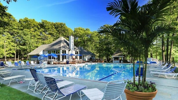 A pool area with lounge chairs, a gazebo, and a building with a chimney.