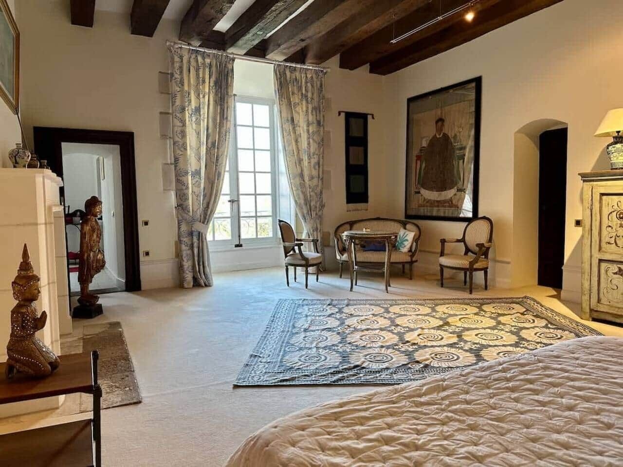 Ein Schlafzimmer mit Bett, Stuhl, Tisch und einem Fenster mit Vorhängen.