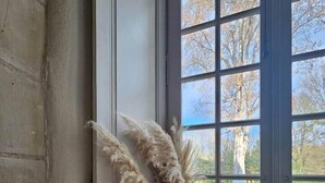 Una habitación con un ventanal grande, una cesta de mimbre con cojines y una puerta.