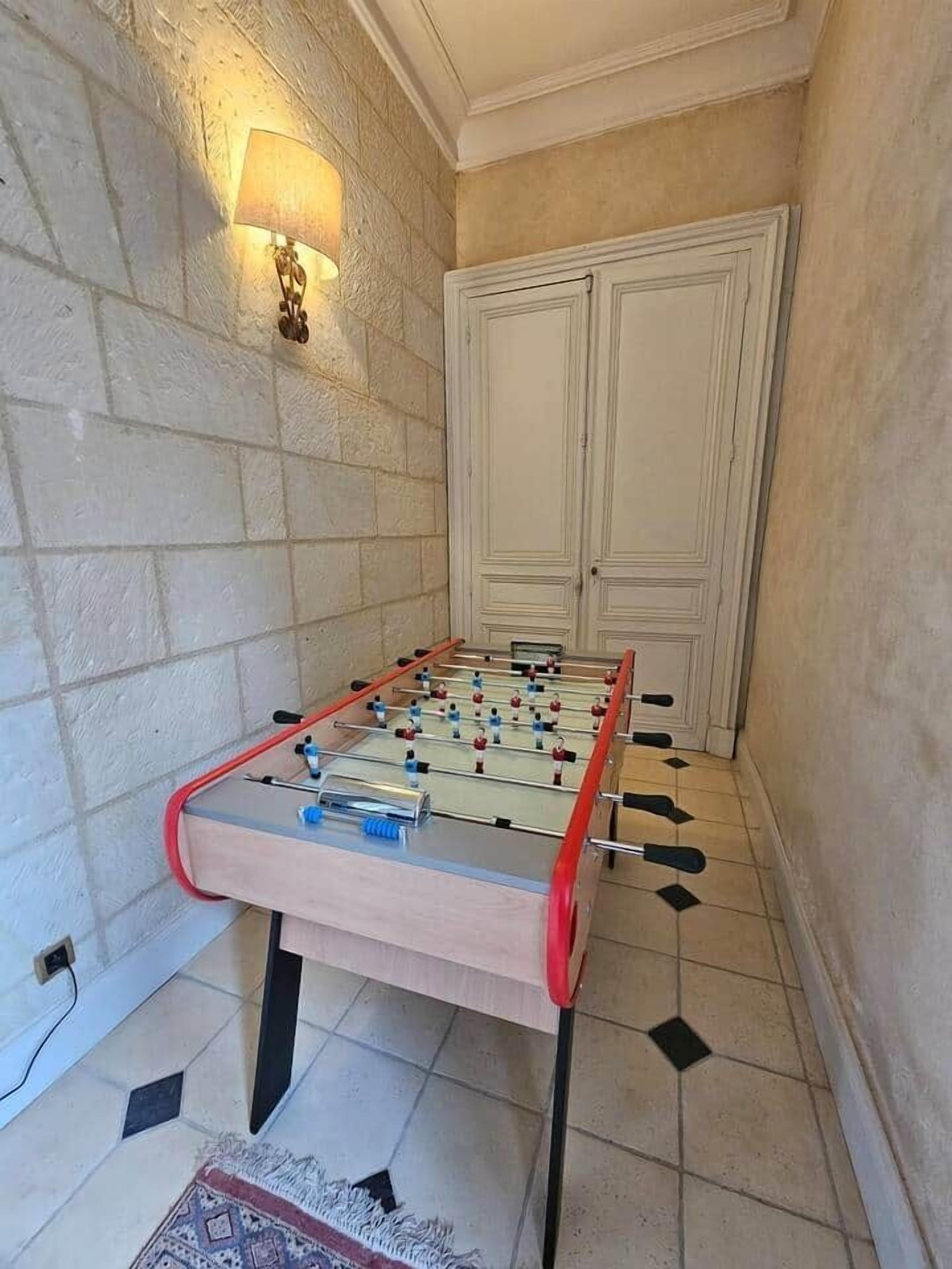Ein Tischkicker in einem Raum mit Steinwänden, Fliesenboden und einer Tür.