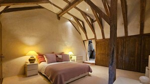 Un dormitorio con techo inclinado, vigas de madera, cama con ropa de cama rosa, lámparas de noche y una pequeña mesa con una figurita de tortuga.