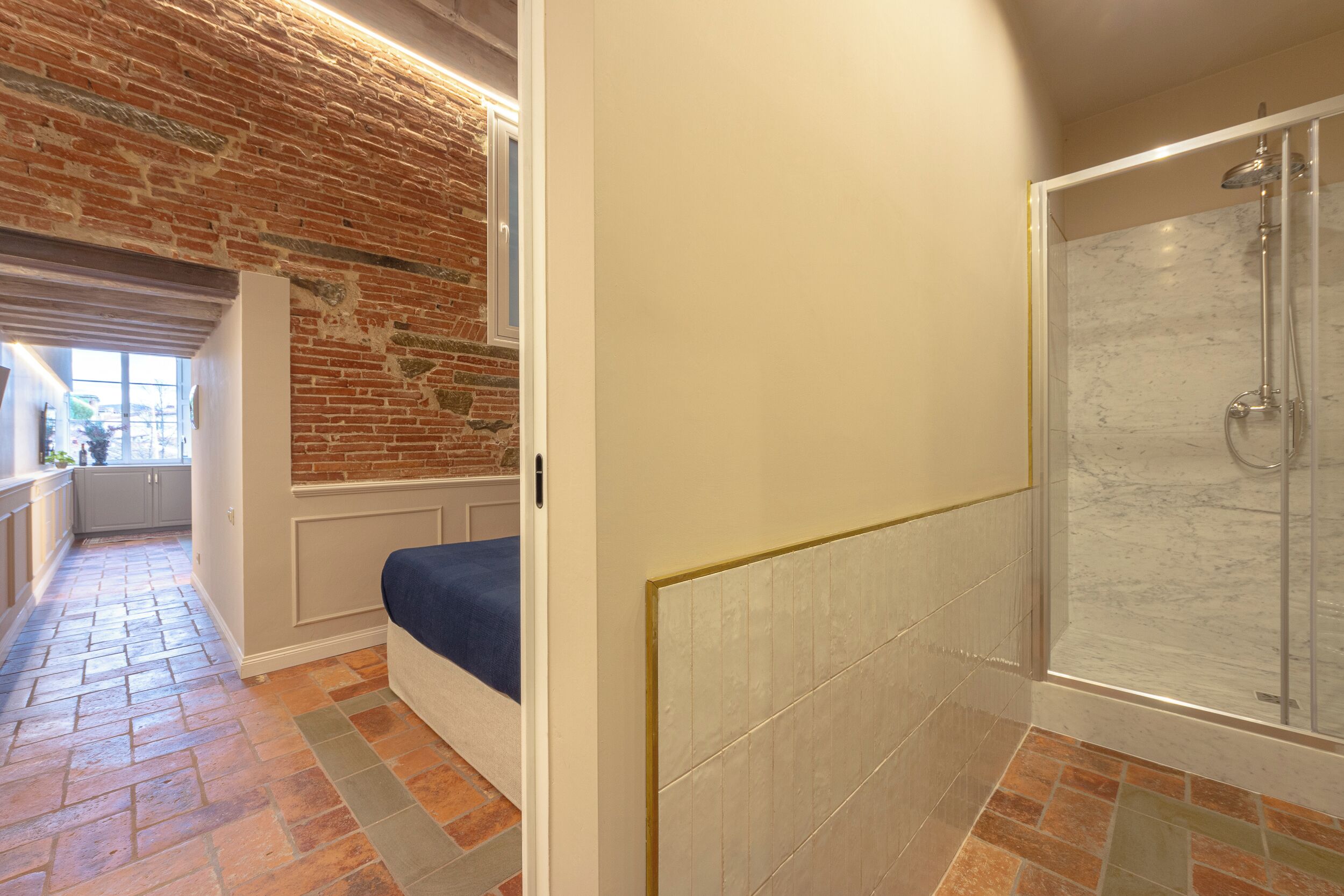 Un baño con ducha, un banco y vistas a una pared de ladrillo y una ventana.