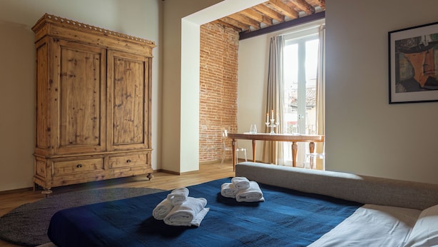 Une chambre avec une grande armoire en bois, un lit avec une literie bleue et une vue sur la ville par la fenêtre.